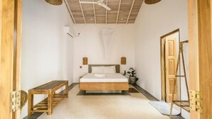 A bedroom with a bed, a wooden bench, a ceiling fan, and a door. - Little House by Unrushed (Ahangama)