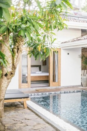 Area piscina con un letto, una sedia a sdraio e un albero.