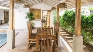 An indoor patio with a wooden ceiling, a ceiling fan, a dining table with chairs, and a view of greenery outside. - Little House by Unrushed (Ahangama)