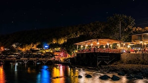 Un restaurante frente al mar con terraza al aire libre, una cubierta de madera y vistas al agua.