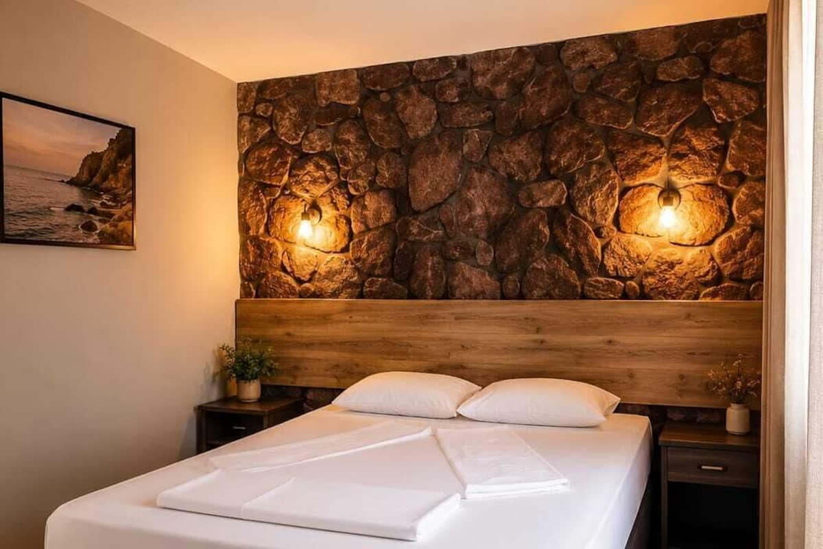 A bedroom with a stone wall, a wooden headboard, a bed with white linens, and two bedside lamps.