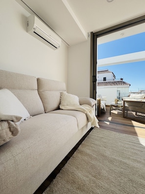 Ein modernes Wohnzimmer mit Sofa, Couchtisch und Blick auf ein Gebäude durch eine Glastür.