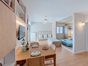 Ein modernes Wohnzimmer mit Essbereich, einem an der Wand befestigten Fernseher, einer Couch und einem Bett.