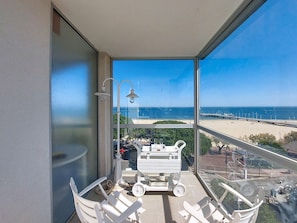 Ein Balkon mit Blick auf den Strand, einem Tisch mit Stühlen und einem Wagen.