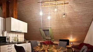 A dining area with a wooden table and chairs, a kitchen in the background, and a wooden ceiling. - Gästehaus Roensch (Frensdorf)