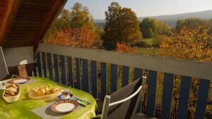 A balcony with a table set for a meal, overlooking a scenic landscape with autumn foliage. - Gästehaus Roensch (Frensdorf)