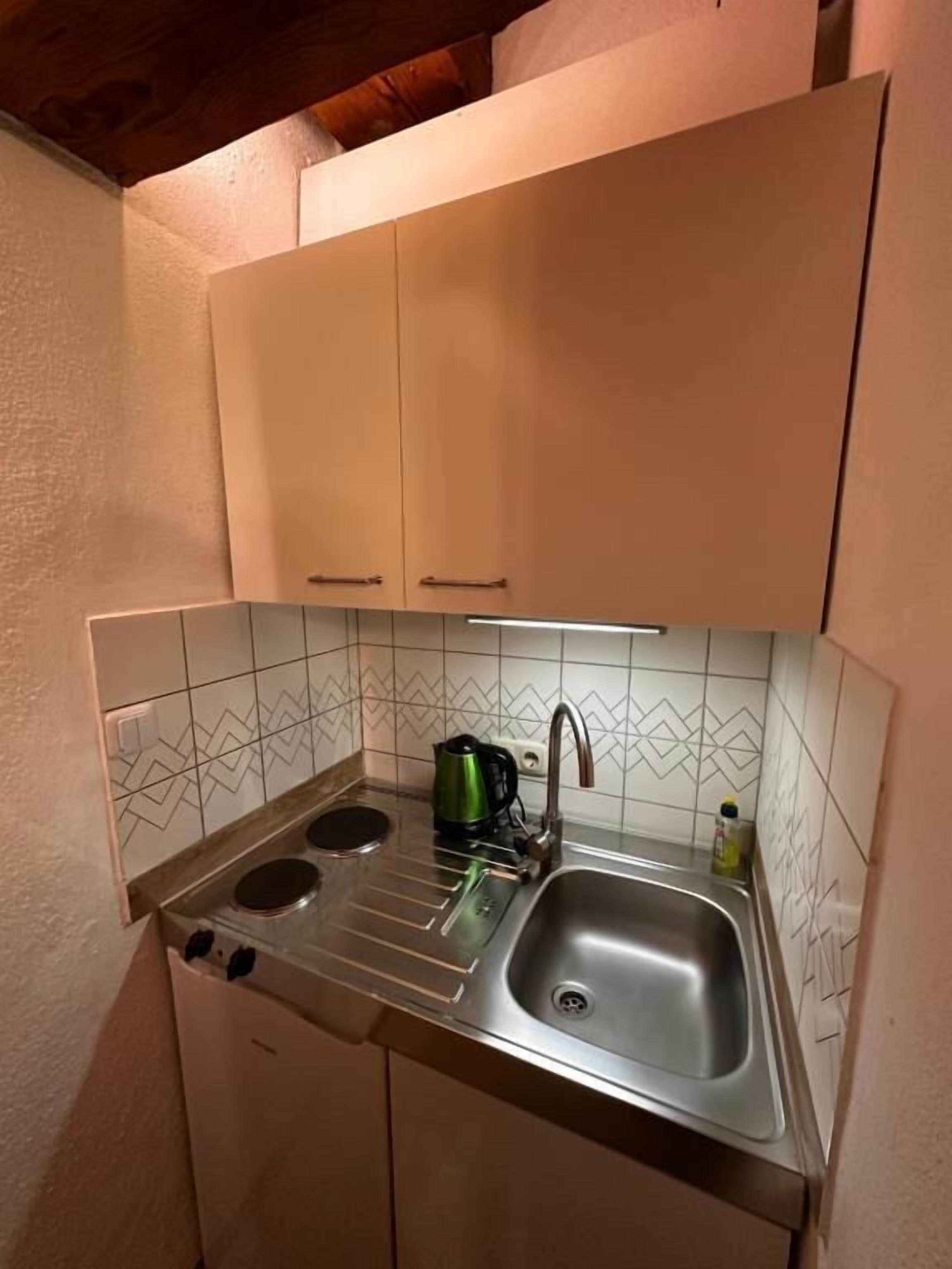 Cocina compacta con dos hornillas, un lavamanos y una tetera.