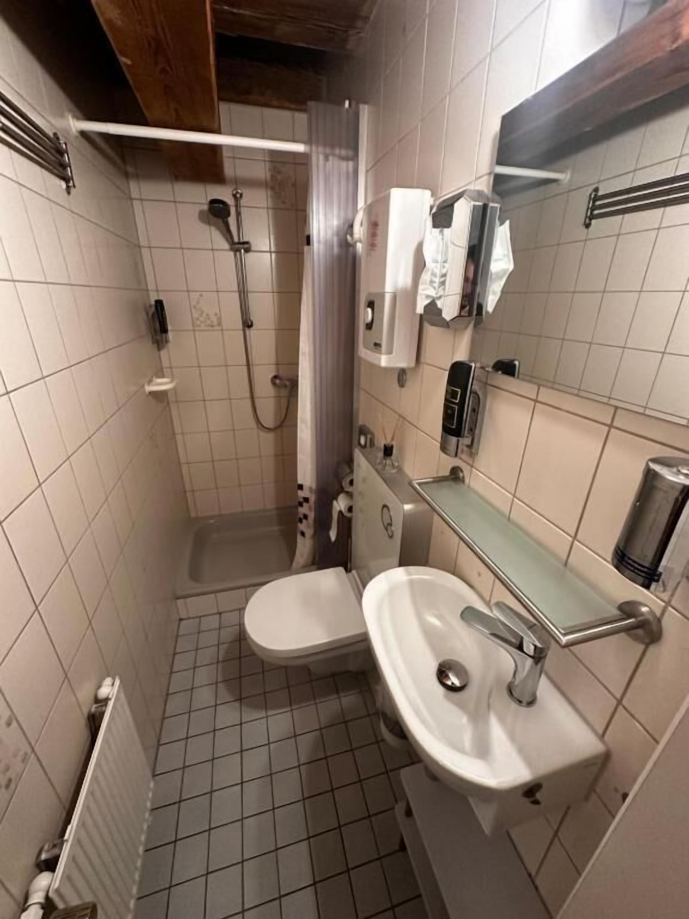 Un bagno piccolo rivestito di piastrelle, con doccia, WC e lavandino.