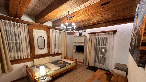 A cozy room with a wooden ceiling, a bed with a headboard, a table, and a chair. - Gästehaus Roensch (Frensdorf)