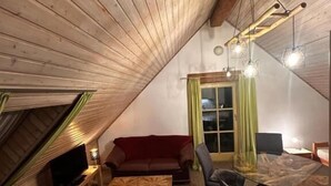 A cozy attic room with a wooden ceiling, a TV, a red sofa, a glass dining table, and a chair. - Gästehaus Roensch (Frensdorf)