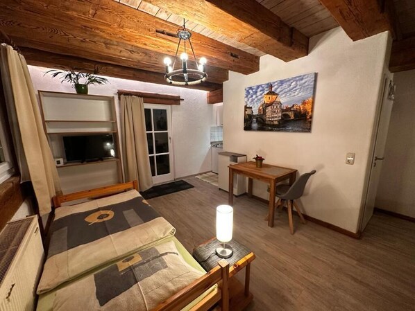 Una habitación acogedora con cama, escritorio, silla, lámpara, un cuadro y televisor.