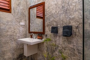 Un baño con pared de mármol, un lavabo blanco, un espejo y un perchero con dos toallas.