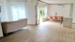 A spacious room with a large window, a sofa, a dining table with chairs, and a marble accent piece.