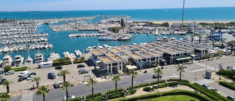A marina with numerous boats docked, a parking area, and a road with palm trees.
