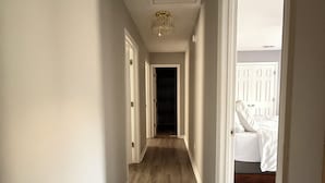 A hallway with wooden flooring, white walls, and a chandelier. There are doors on both sides leading to other rooms. - Quiet Fully Furnished Comfy Home with Fast WiFi for Professionals in RTP/Durham (Durham)