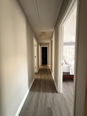 Ein Korridor mit Holzboden, weißen Wänden und einem Chandelier. Auf beiden Seiten befinden sich Türen zu weiteren Räumen.