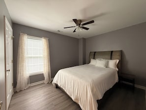 Ein Schlafzimmer mit Bett, Deckenventilator, Fenster mit Vorhängen und einer Tür.