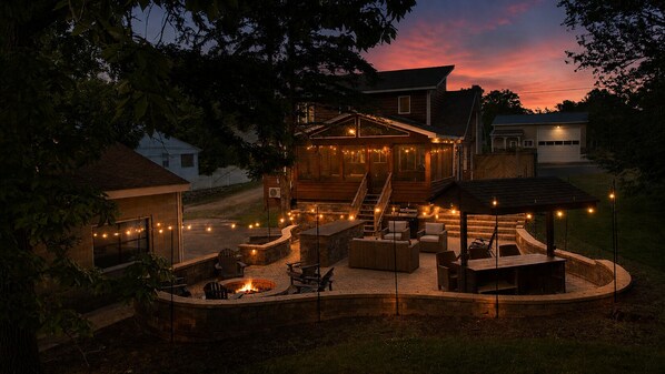 A well-lit outdoor patio area with a fire pit, seating, and string lights.