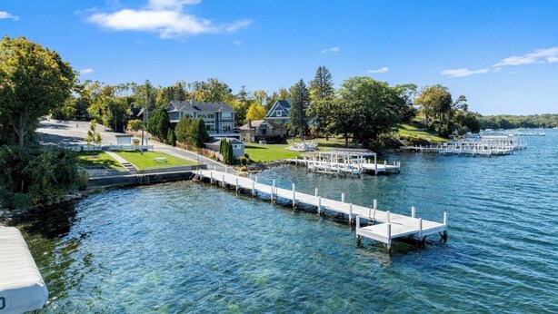 A waterfront property with a dock, clear water, and houses in the background. - Linn Lodge | Fire Pit, 5+ Night Stays Include Golf Cart | Sleeps 10 (Lake Geneva)