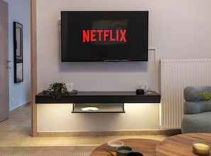 Ein modernes Wohnzimmer mit einem an der Wand montierten Fernseher, der 'NETFLIX' anzeigt, einem Holz-Konsolentisch mit Dekoration, einer Couch und einem Couchtisch.