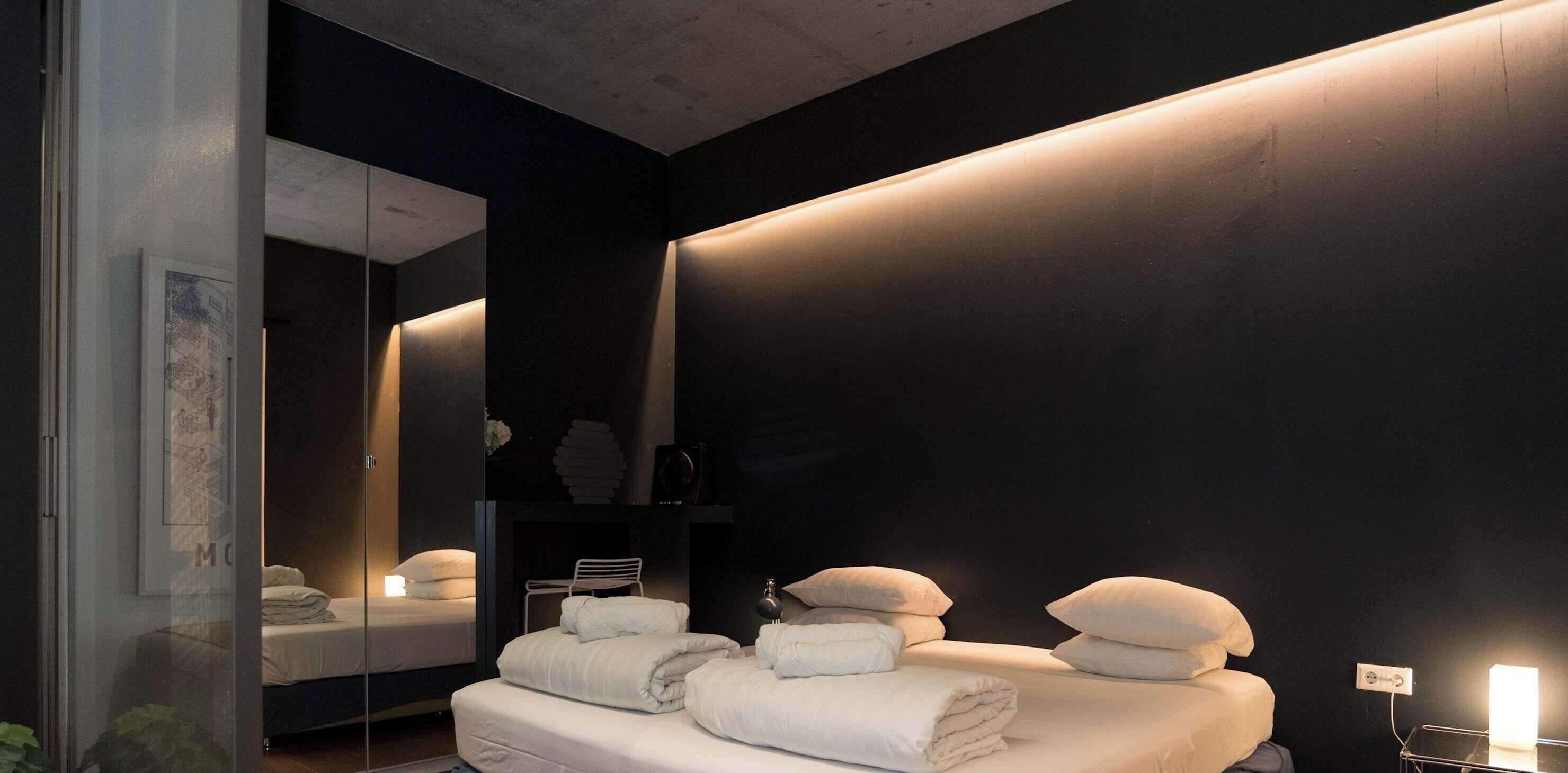 Un dormitorio moderno con una cama grande, mesitas de noche, un espejo y una lámpara fijada a la pared.