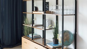 Una habitación con una estantería alta y abierta que contiene diversos objetos como libros, cristalería y adornos.