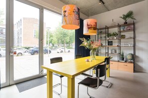 Une piĂšce lumineuse avec une table jaune, des chaises noires, une bibliothĂšque et une vue sur la rue.