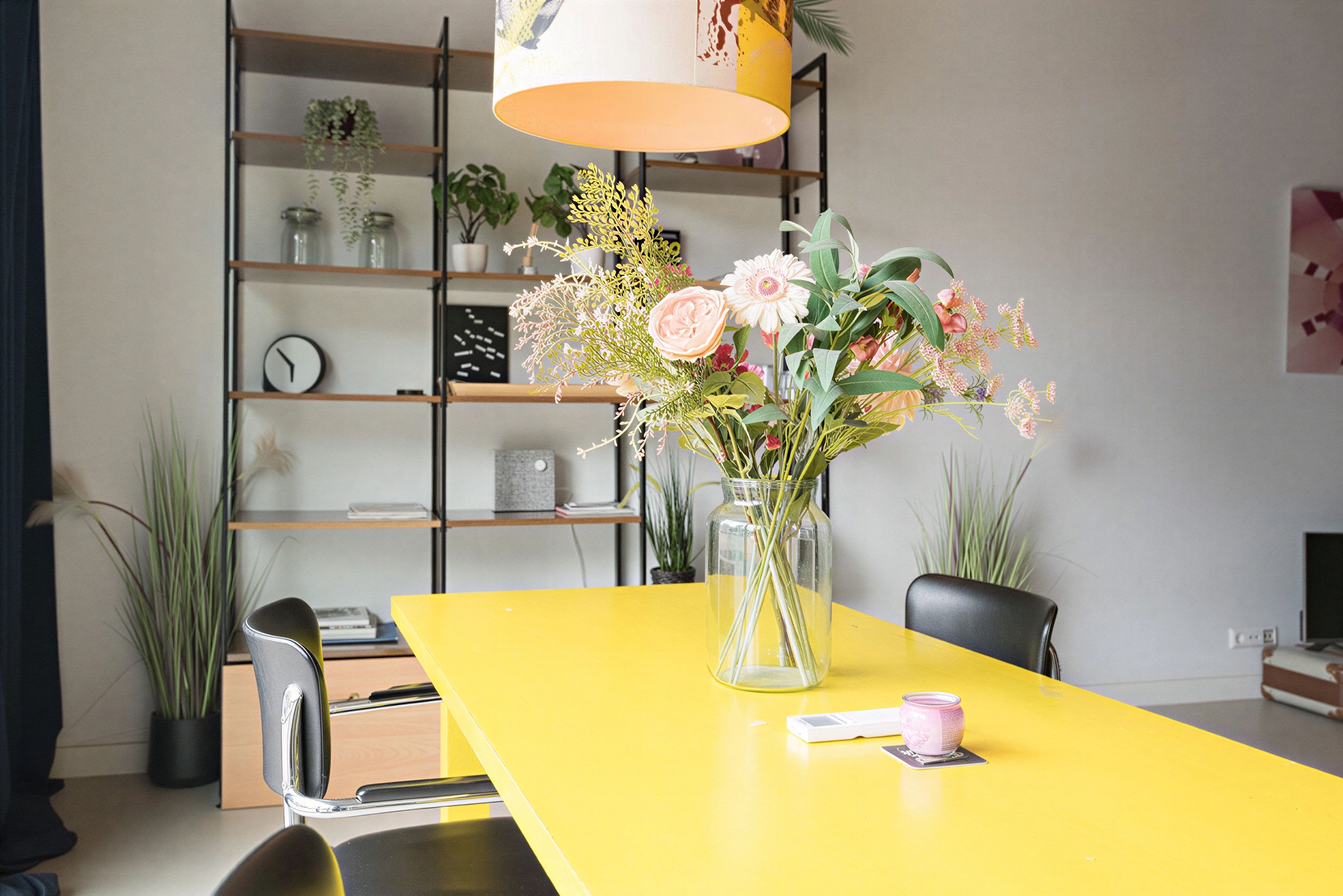 Una mesa de comedor amarilla con un jarrón de flores en el centro.