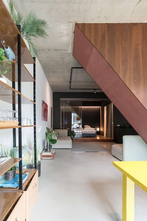 Een modern interieur met een trap, een bank, een gele tafel en een boekenkast met planten.