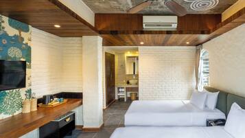 A hotel room with a wooden ceiling, a flat-screen TV, a brick wall, a bed, and a bathroom visible through an open door.