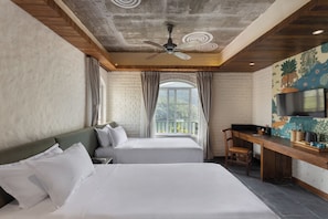 Habitación de hotel con dos camas, un escritorio, un ventilador de techo y un ventanal grande con cortinas.