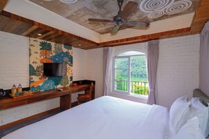Una habitación de hotel con una cama, un escritorio con televisor, una ventana con vistas y un ventilador de techo.