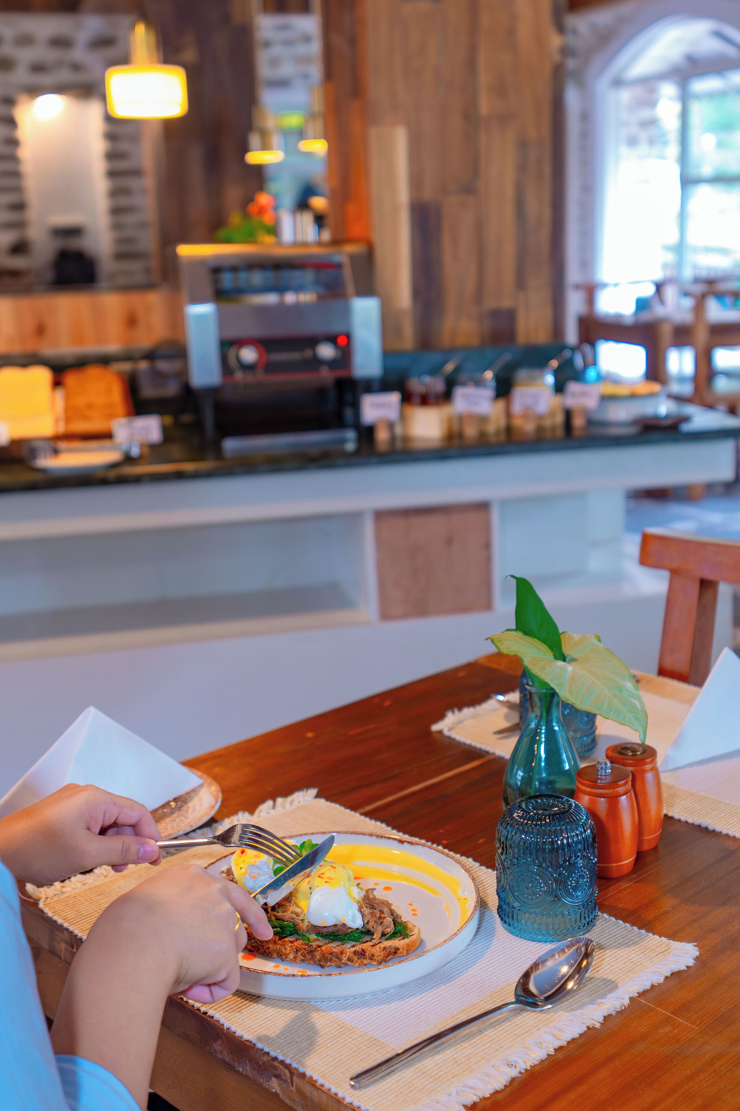 A dining table with a plate of food, a blue vase with a plant, and a coffee machine in the background.