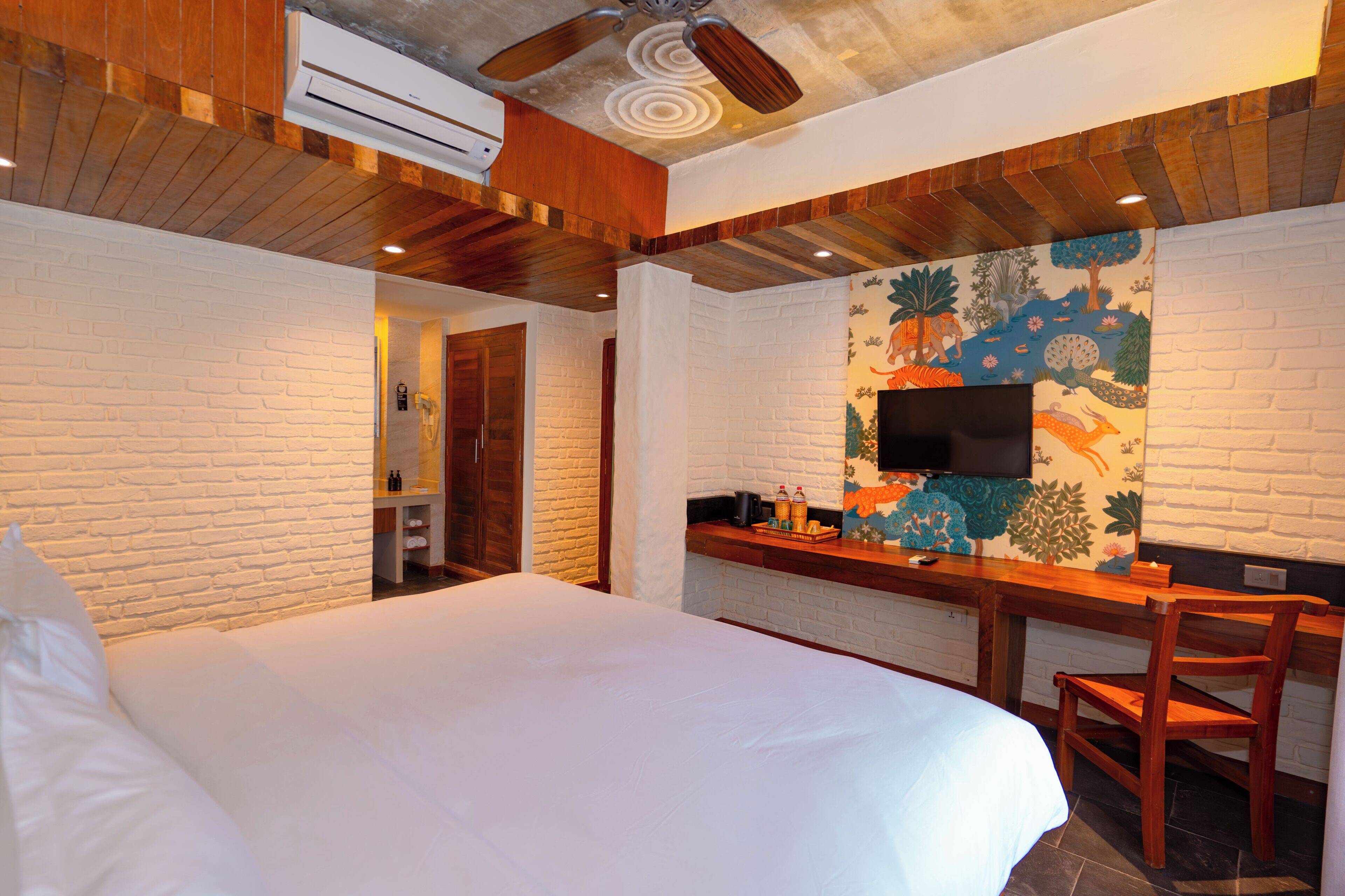 A hotel room with a bed, a desk with a flat-screen TV, and a shower area.