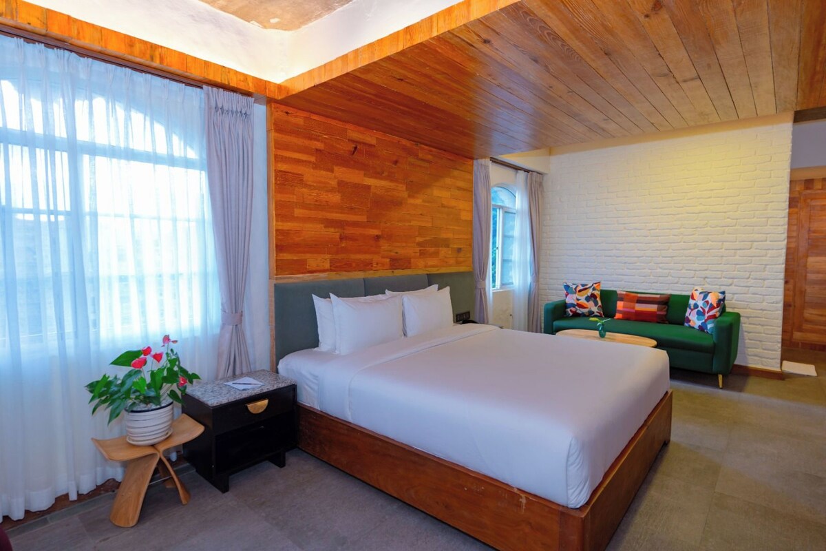 A bedroom with a wooden headboard, a bed with white bedding, a green sofa, and a small table with a plant.