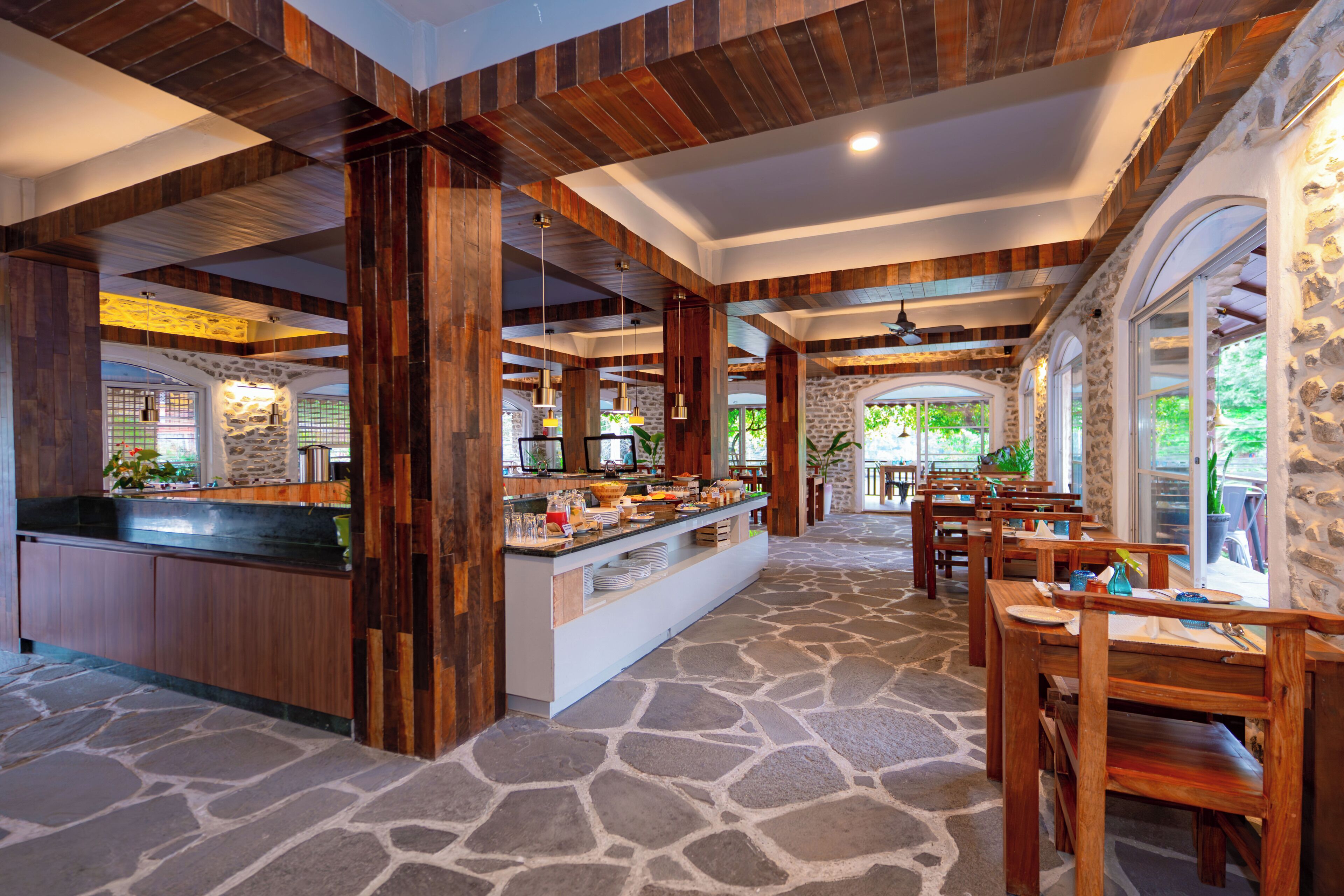 A restaurant with a stone floor, wooden furniture, and a buffet area.
