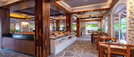 A restaurant with a stone floor, wooden furniture, and a buffet area.