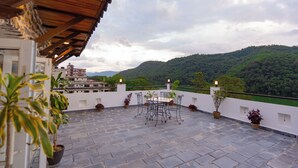 A terrace with a table and chairs, potted plants, and a view of a mountain range. - Nomad Pokhara Hotel  (Pokhara)