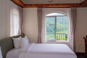 Una habitación con cama, ventana con cortinas y vistas a un área boscosa.