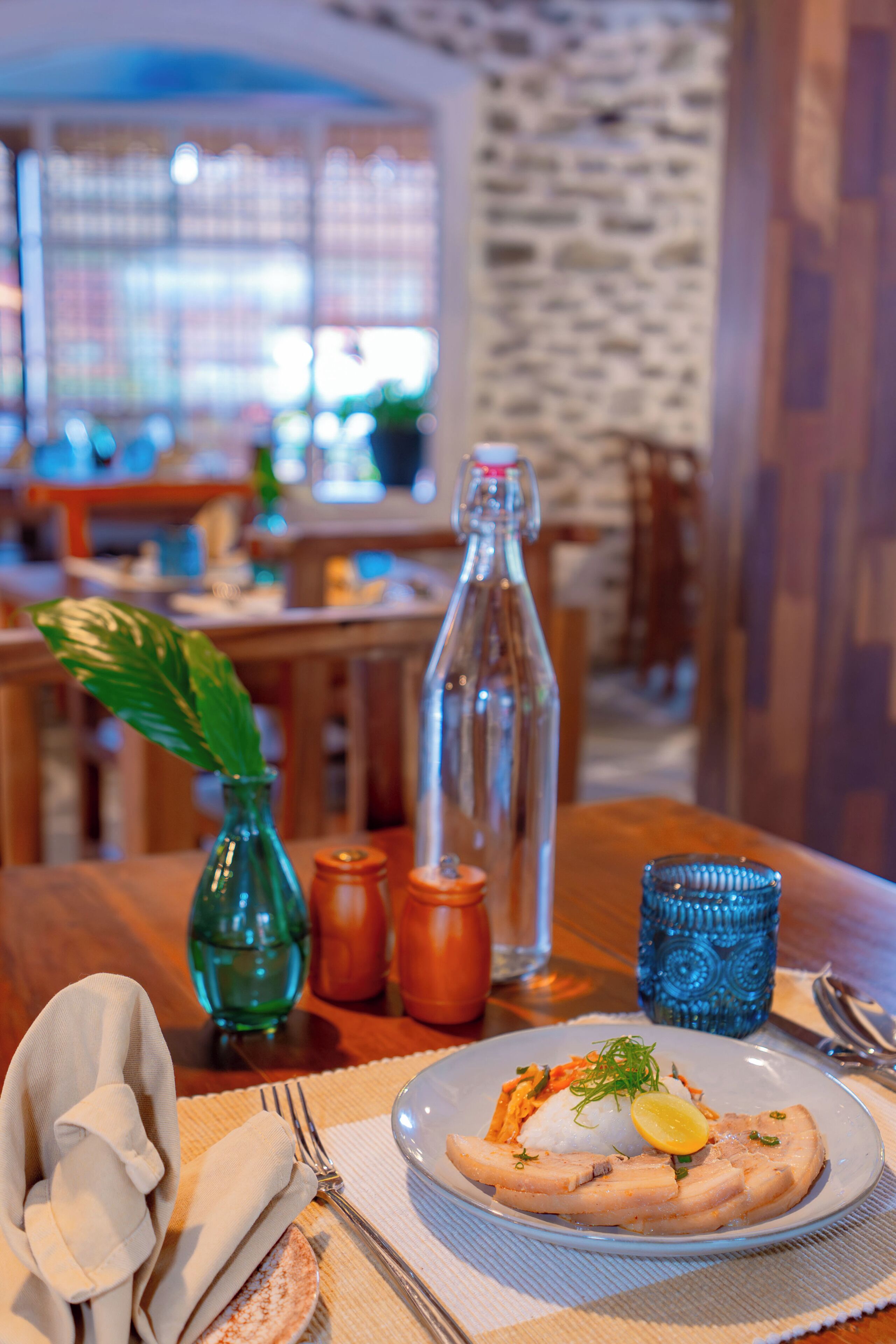 A dining table with a plate of food, a glass bottle, and a decorative vase.