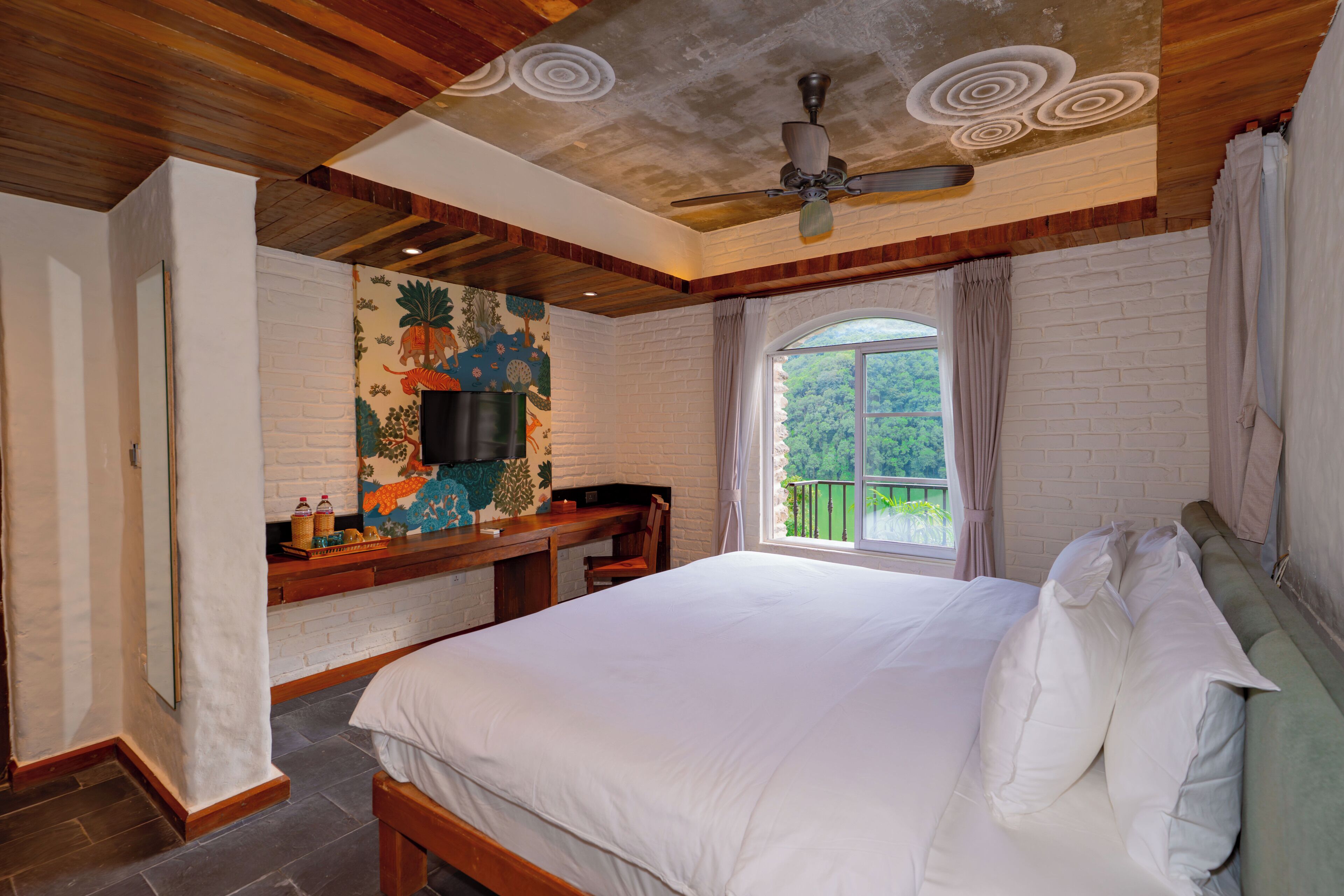 Un dormitorio con una cama grande, un ventilador de techo, una ventana con cortinas y una pared con un mural.