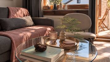 Ein modernes Wohnzimmer mit einem Glastisch, einer Couch, einem Sessel und Blick auf einen Berg.