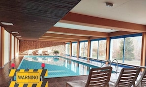 Ein Hallenbad mit freiem Blick ins Freie, einer Holzbalkendecke und Liegestühlen am Pool.