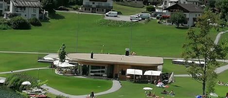 A lakeside hotel with a central building, a dock, and a grassy area with umbrellas.
