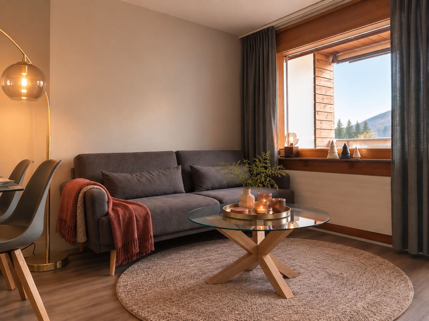 Ein modernes Wohnzimmer mit einem grauen Sofa, einem Glastisch und Blick auf einen Berg durch ein Fenster.