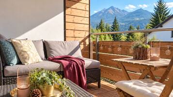 Ein Balkon mit einer Couch, einem Sessel und einem Tisch mit Pflanzen und einem Kerzenständer.