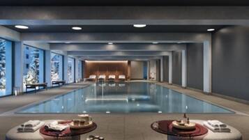 Ein moderner, überdachter Schwimmbereich mit Liegestühlen und Tischen, umgeben von Wänden mit großen Fenstern.