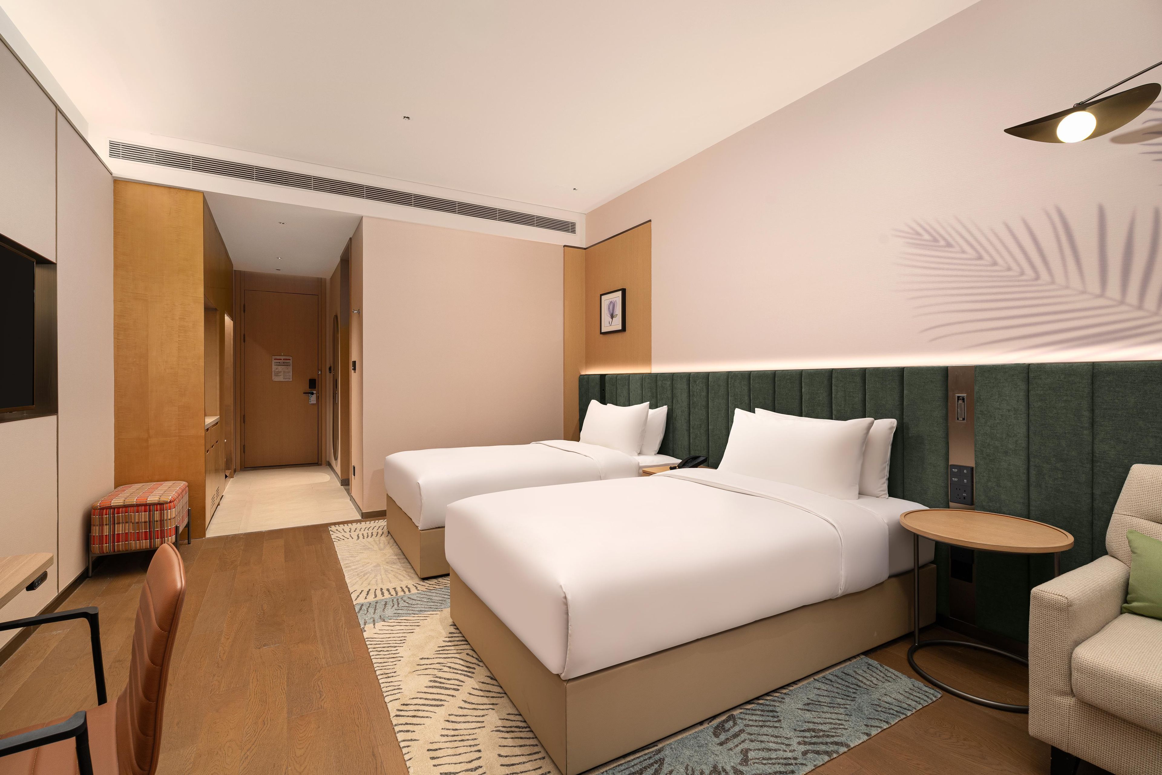 Une chambre d’hôtel avec deux lits, un bureau, une chaise, une petite table et une lampe fixée au mur.