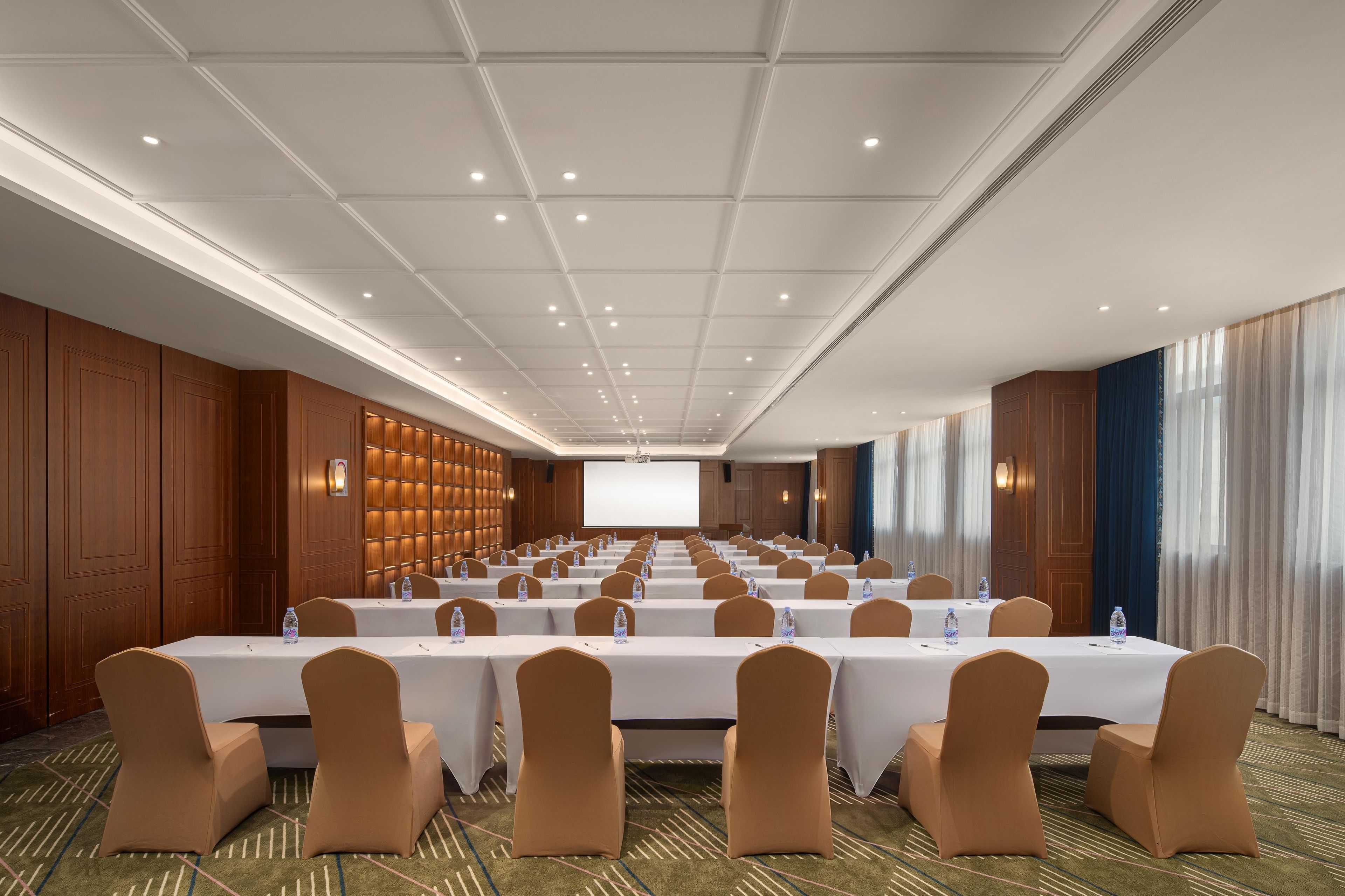 A conference room with rows of tables and chairs, a projector screen, and a large screen for presentations.