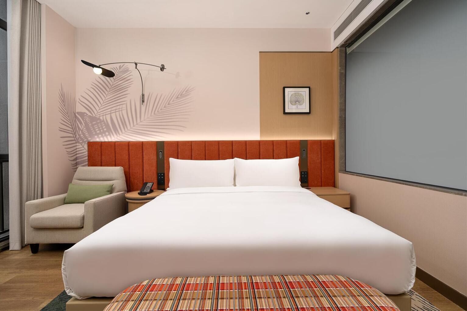 A hotel room with a large bed, a chair, a nightstand, a lamp, and a framed picture on the wall.